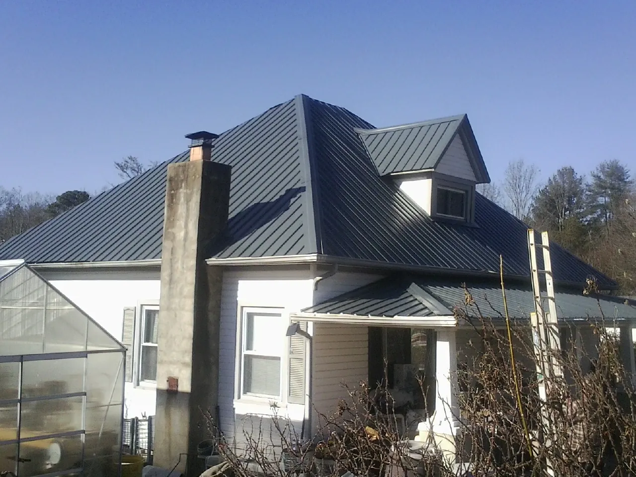 Dark blue standing seam metal roof on a white farmhouse with dormer — Slate & Tile Roof Repair by Roofing Brothers in Jefferson Valley