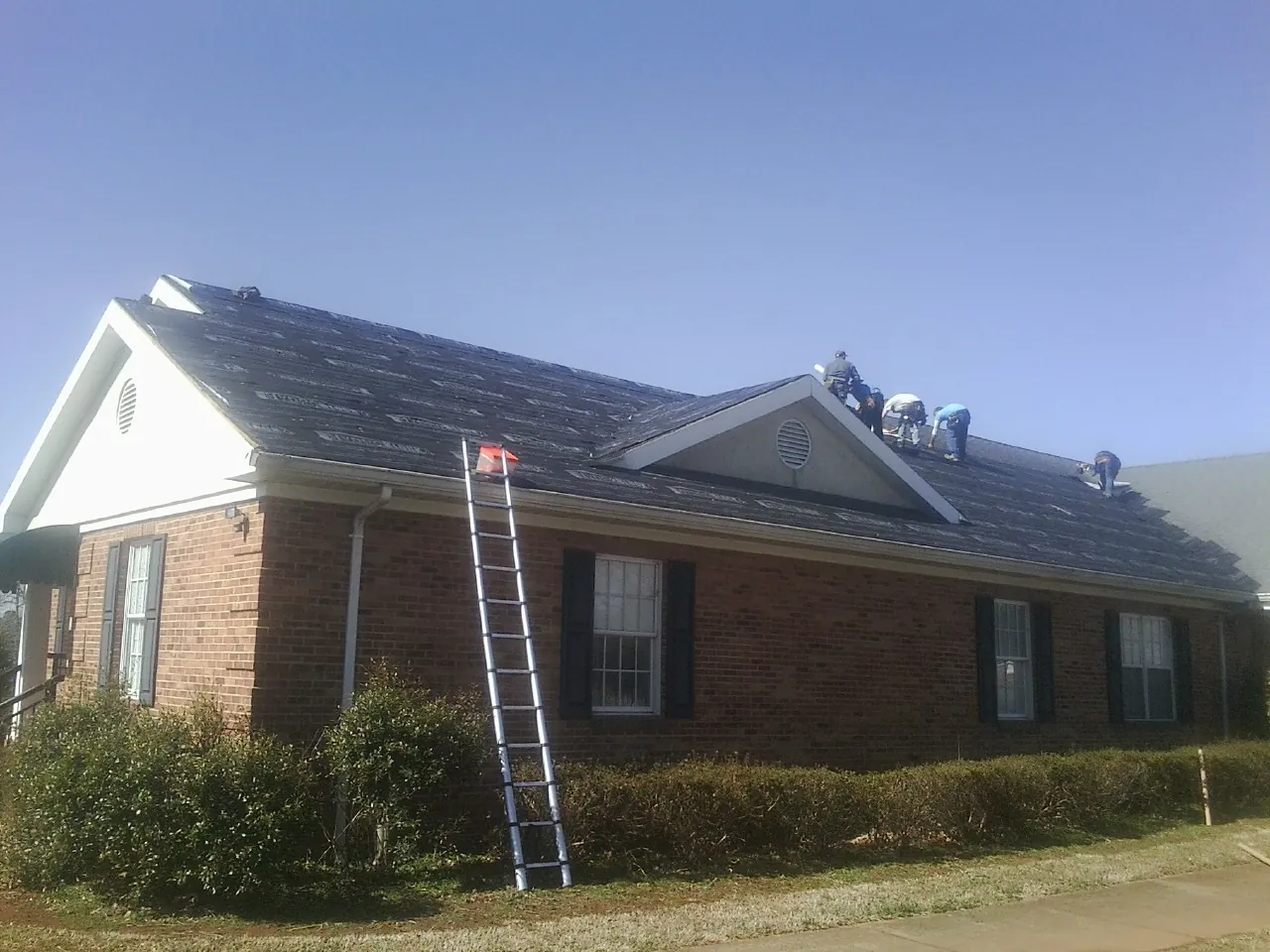 Crew tearing shingles off a brick ranch roof with a ladder set — Metal Roof Repair work by our crew in Jefferson Valley