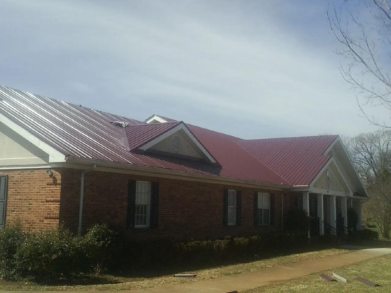 Red metal roof with gabled entries on a long brick building, from a Hail Damage Roof Repair job in Jefferson Valley