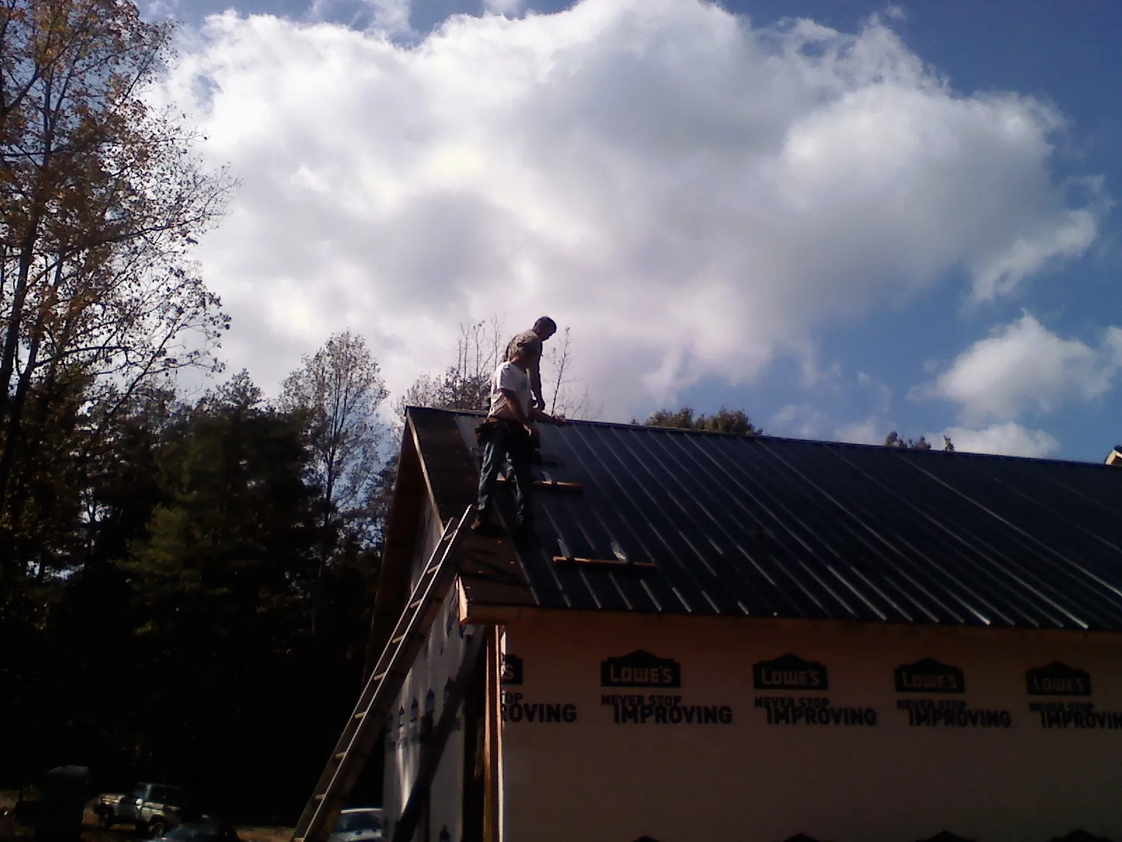 Roofer fastening dark metal panels high against a cloudy sky, from a Roof Inspection job in Jefferson Valley