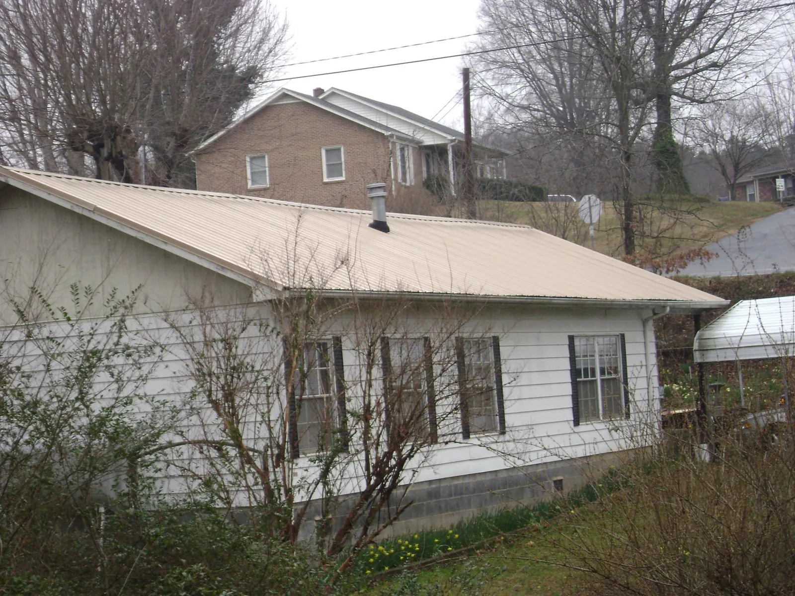 Tan metal roof on a white sided house set into a hillside — Commercial Roofing by Roofing Brothers in Jefferson Valley
