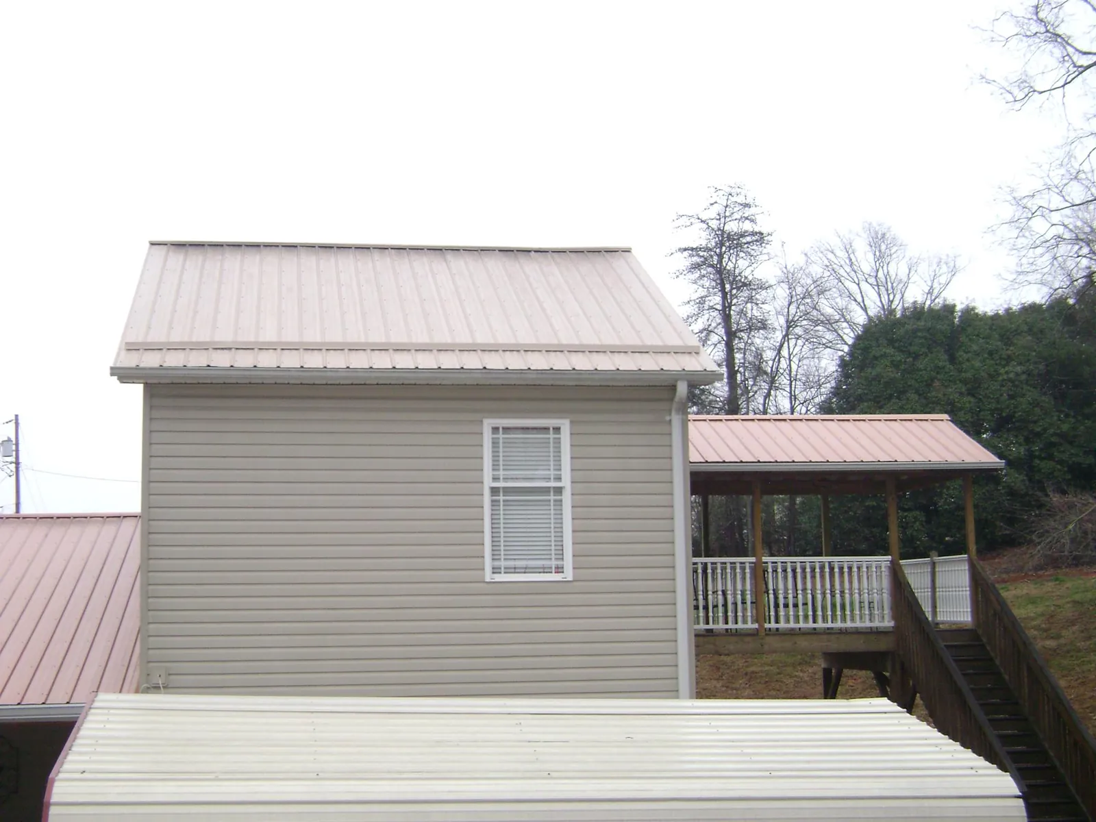 Tan metal roofs on a two story addition and attached porch, from a Roof Replacement job in Jefferson Valley