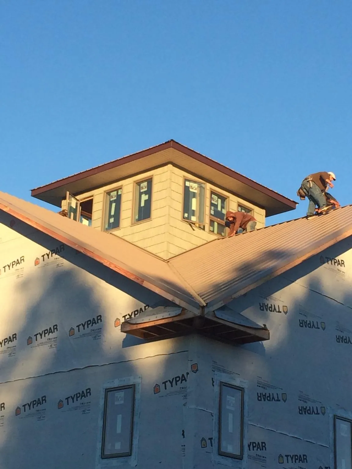 Roofers working around a rooftop cupola on a new metal roof at sunset — Roof Waterproofing in Jefferson Valley by Roofing Brothers